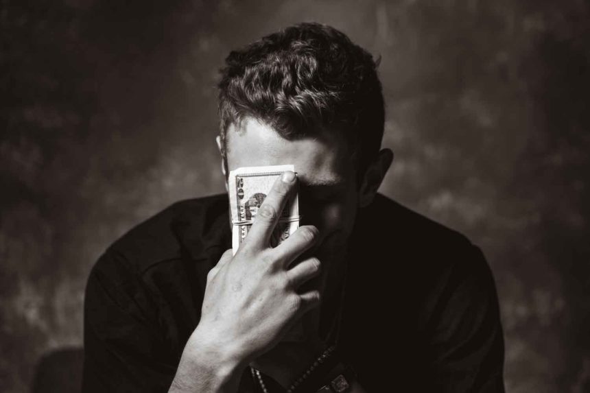 A man with a thoughtful expression holding cash to his forehead, reflecting on Law of Attraction Money strategies.