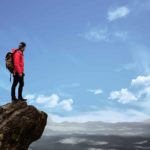 Persistence Is One of the Fundamental Factors of Success. Man on top of the mountain looks at clouds.