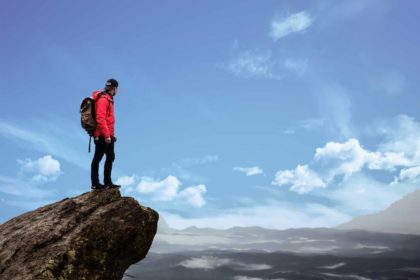 Persistence Is One of the Fundamental Factors of Success. Man on top of the mountain looks at clouds.