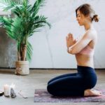 A woman sitting on a yoga mat with hands together practicing rituals.