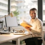 A man sitting at a desk in office holding a book