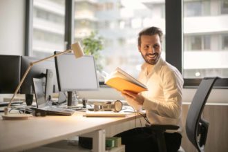 A man sitting at a desk in office holding a book